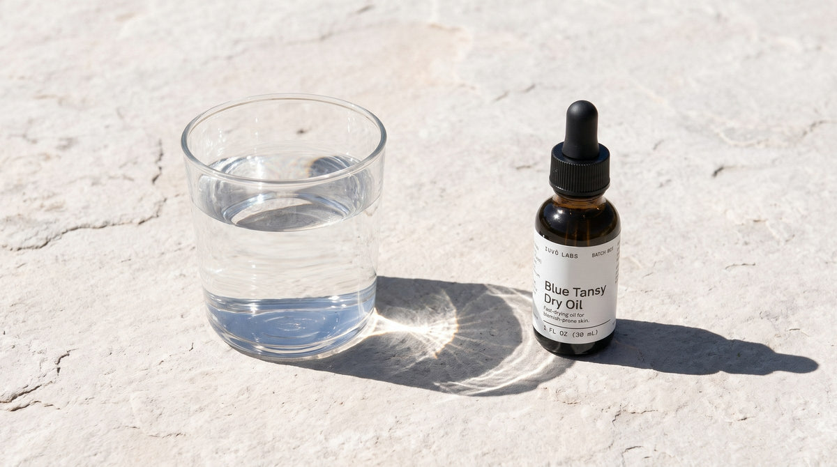 Blue Tansy Dry Oil beside a glass of water on pale stone